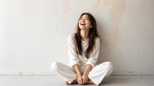 白い壁の前に座り自然に笑う健康的な女性 no.1