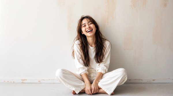 白い壁の前に座り自然に笑う健康的な女性 no.3