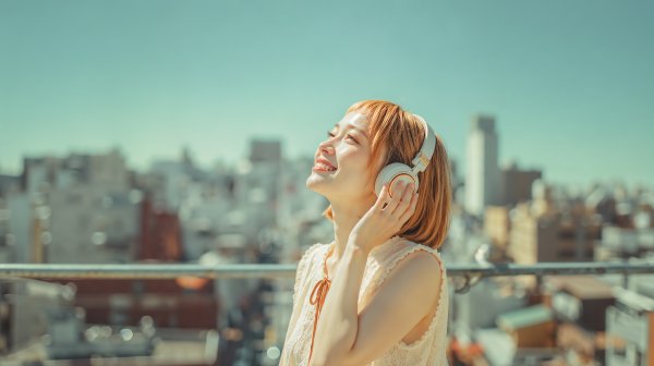 ヘッドホンで音楽を聴きながら都会の空を見上げる笑顔の女性 no.1